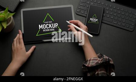 Top view of female working on mock up digital tablet on black table with mock up smartphone and keyboard Stock Photo