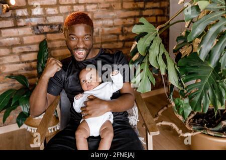 Happy loving black father holding cute african kid, laughing cuddling small son sit on chair, cheerful little child boy laing on the dad hands Stock Photo