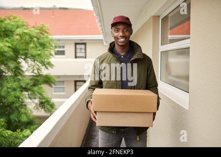 Smiling African delivery man standing outside carrying packages Stock Photo