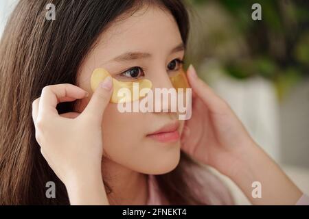 Close-up image of woman applying moisturizing patches under eyes of her pretty friend Stock Photo