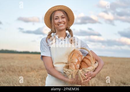 Female farmer standing wheat agricultural field Woman baker holding wicker basket bread eco product Baking small business Caucasian person dressed str Stock Photo