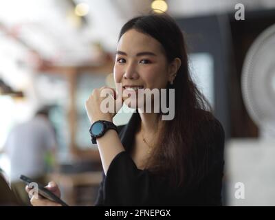 Portrait of young businesswoman in black suit wearing smartwatch, smiling and looking into camera Stock Photo