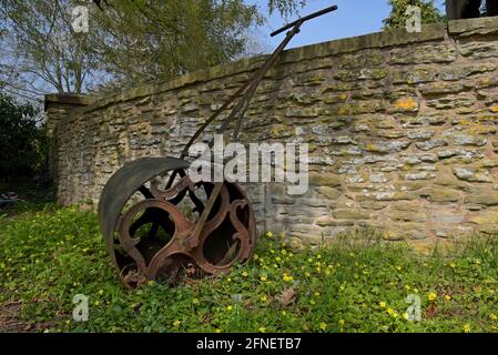 A rusty vintage iron garden lawn roller leaning against the wall in Chelmarsh churchyard, Shropshire, UK Stock Photo