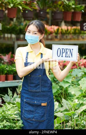 Lovely young woman wearing protective mask when inviting customers in gardening center Stock Photo
