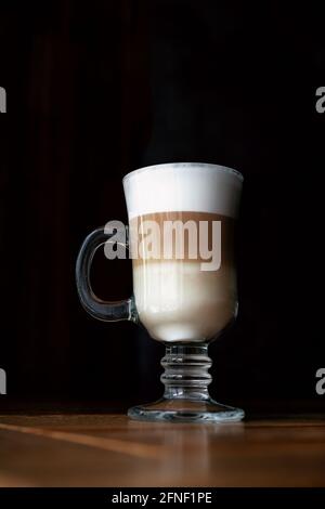 Coffee latte in a glass cup with black background. Three-layer latte on a dark background. Coffee latte in a glass cup with black background. Coffee with milk. Vertical shot. Stock Photo