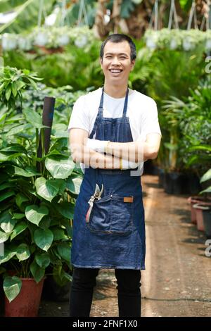 Portrait of happy confident young man standing in plant nursery, crossing arms and looking at camera Stock Photo