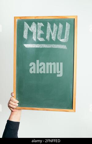 vertical photo of a hand holding a chalkboard with the word MENU handwritten in chalk, copyspace for text Stock Photo
