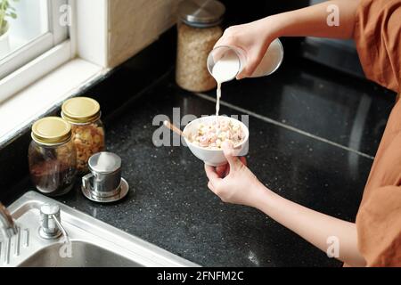 Woman pouring fresh milk in bowl of muesli and cornflakes for breakfast Stock Photo