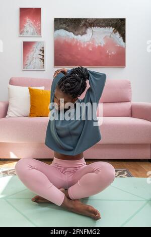 Fit African American female sitting on mat and stretching arms while warming up before workout at home Stock Photo
