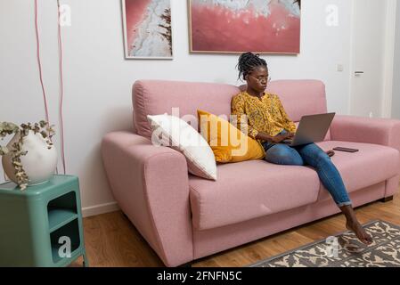Concentrated black bussineswoman freelancer working on startup project and sitting on couch in living room Stock Photo