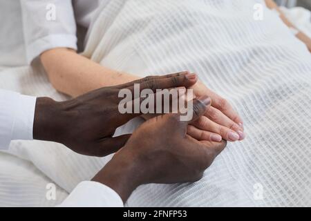 Close-up of African doctor holding hand of his patient at hospital Stock Photo