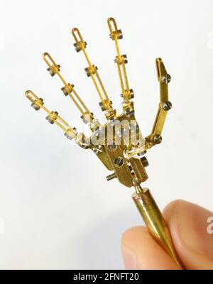 15 May 2021, Saxony, Leipzig: In his small workshop, the Leipzig computer science student and filmmaker Valentin Felder holds between his fingers a hand about 5 centimeters small for his half-hour film 'Gear in the Sand'. He has already turned, filed, soldered and milled thousands of parts, ranging in size from 0.5 millimetres to a few centimetres, made of copper, brass, wood, steel, plaster or polystyrene for his robots and machines. He documents the development of this creative project, which should be finished in three years at the latest, online and receives small donations from all over Stock Photo