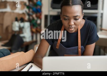 African female leather worker using a laptop in her workshop Stock Photo