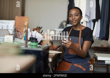 African female leather worker using a tablet in her studio Stock Photo