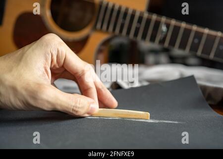 Lower the height of an acoustic guitar saddle for a better playability by sanding down a bone saddle with sandpaper Stock Photo