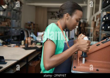 African female leather worker using a cutting machine Stock Photo