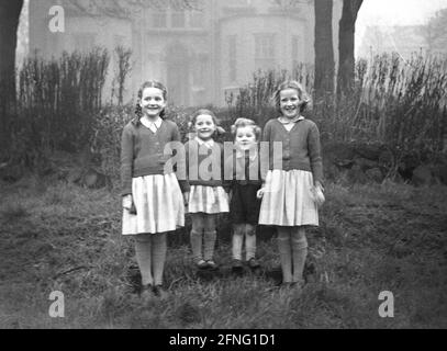 1950s, historica, family picture, big smiles alround as three sisters, in their school clothes stand with their little brother, for a photo, England, UK. Stock Photo