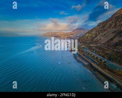 The A55 expressway, old Thomas Telford road and North Wales Railway around the headland at Llanfairfechan, with Penmaenmawr and Llandudno visible. Stock Photo