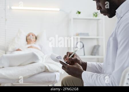 Close-up of African doctor writing prescription in medical card for patient who lying on hospital bed Stock Photo