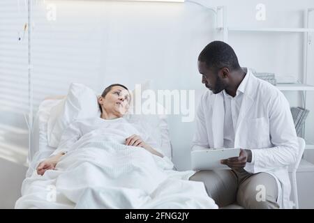African doctor with medical card talking to patient who lying on hospital bed Stock Photo