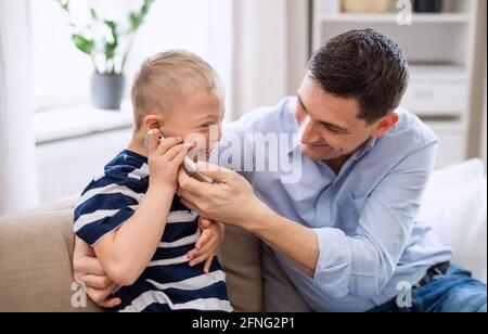 Father with happy down syndrome son indoors at home, using smartphone. Stock Photo