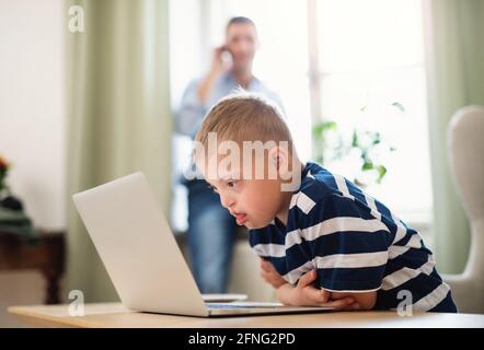 Down syndrome boy with unrecognizable father indoors at home, using laptop. Stock Photo