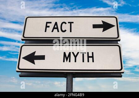 Fact versus myth road sign with two arrows on blue sky background. White two street sign with arrows on metal pole. Two way road sign with text. Stock Photo