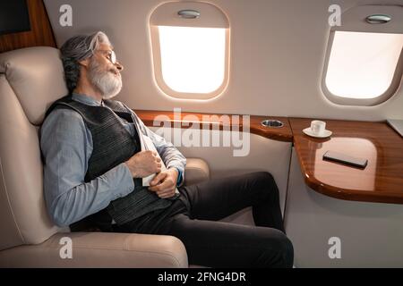Mature businessman with magazine sleeping near cup and smartphone in jet Stock Photo
