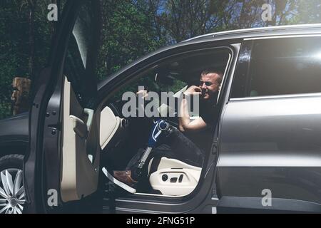 a man on a prosthetic leg sits in a car. Dressed in black jeans and a T-shirt Stock Photo