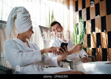 Portrait of young couple relaxing in spa resort, using smartphone. Stock Photo