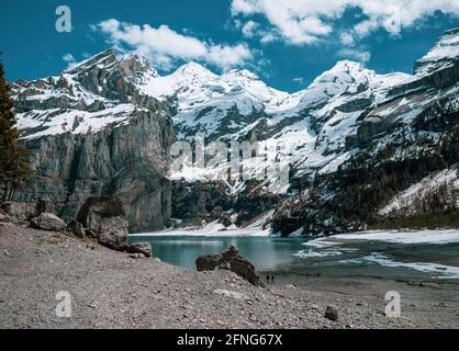 High alpine lake of Oeschinensee in Kandersteg, Switzerland. The picturesque clear blue lake is surrounded by high snow covered mountains, glaciers an Stock Photo