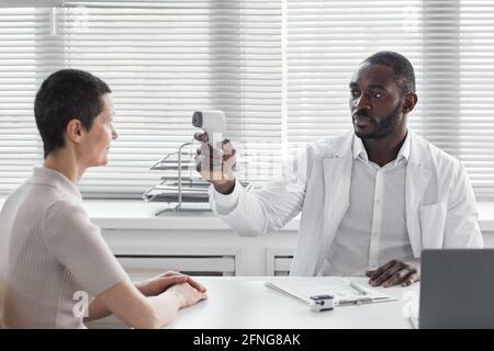 African doctor checking the temperature of his patient during her visit at hospital Stock Photo
