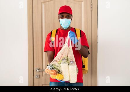 Black delivery man holding eco mesh bag with groceries Stock Photo