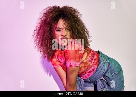 Fit African American female dancer in shorts dancing looking at camera while standing in neon lights in studio Stock Photo
