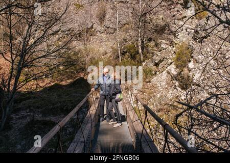 Loving senior man and Woman looking at each other while standing on footbridge against rocky mountains Stock Photo