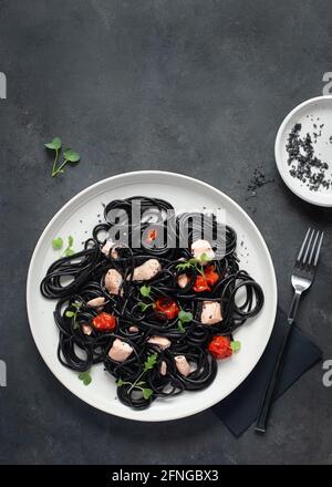From above black ink spaghetti with salmon in ceramic plate on dark background Stock Photo