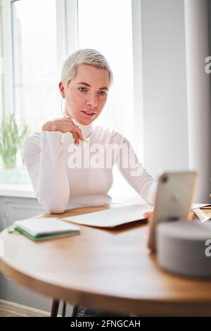 Female blogger talking about astrology while recording video on cellphone at desk in sunlight Stock Photo