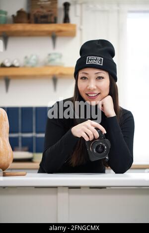 Content ethnic Woman with digital photo device leaning with hand on table while looking at camera Stock Photo
