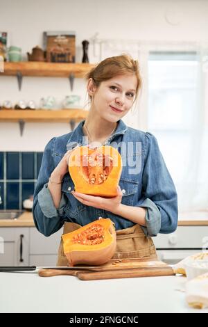 Satisfied female demonstrating half of fresh squash with seeds while looking at camera in house Stock Photo