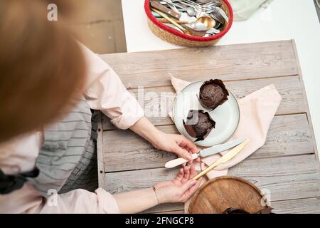 From above of crop unrecognizable female with knives over delicious muffins in baking cups on wooden table in kitchen Stock Photo