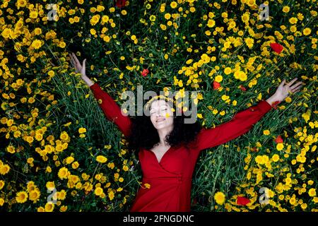 Top view of romantic female in red apparel with closed eyes lying in field among blossoming Papaver and daisies Stock Photo