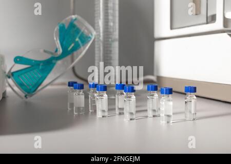 Similar small transparent bottles with liquids against protective glasses on table in cannabis lab Stock Photo