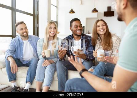 Diverse millennial friends talking and laughing together, drinking tea or coffee at home Stock Photo
