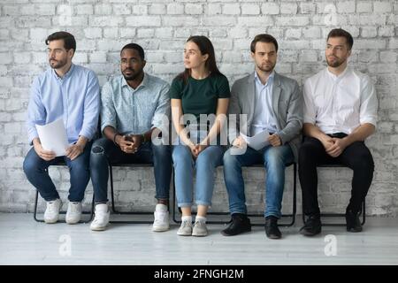 Worried unemployed professionals sitting in queue, holding paper resumes Stock Photo