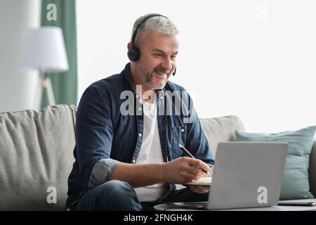 Excited mature man studying online, using laptop and headset Stock Photo