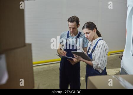 Young woman in uniform using tablet pc and working with her colleague while they working in warehouse Stock Photo