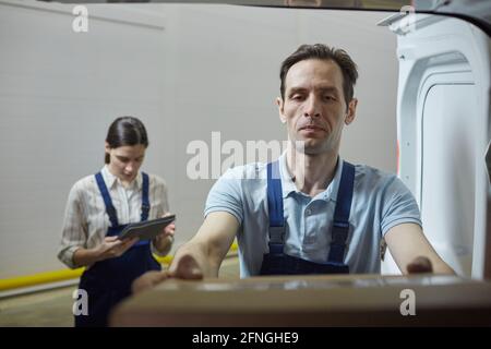 Young man shipping the box in the lorry with woman registrating it in the background Stock Photo