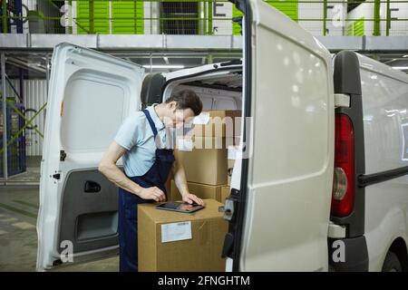 Young man in uniform registrating parcel with digital tablet before delivery Stock Photo