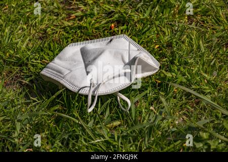 A white face mask lies lost on a green area and pollutes nature Stock Photo