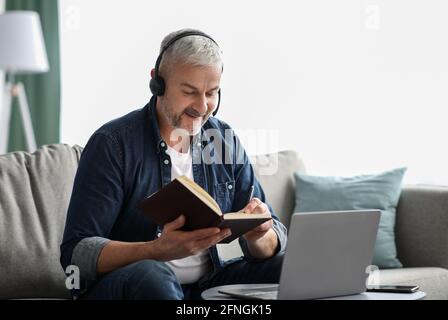 Happy old man having online class, using laptop and headset Stock Photo